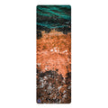 A tall, narrow yoga mat featuring an abstract coastal or watercolor design with teal, orange, brown, black, and white tones, shown on a plain white background.