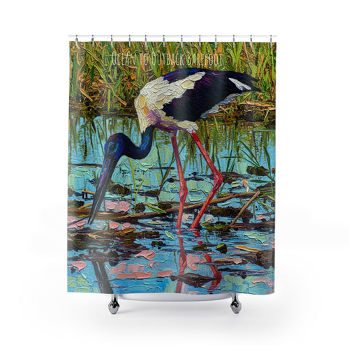 A shower curtain featuring a colourful painted scene of a black-necked stork with red legs standing in shallow water, with the text 'OCEAN TO OUTBACK BAREFOOT' across the top. The curtain is shown hanging from silver rings on a white rod against a light gray background.