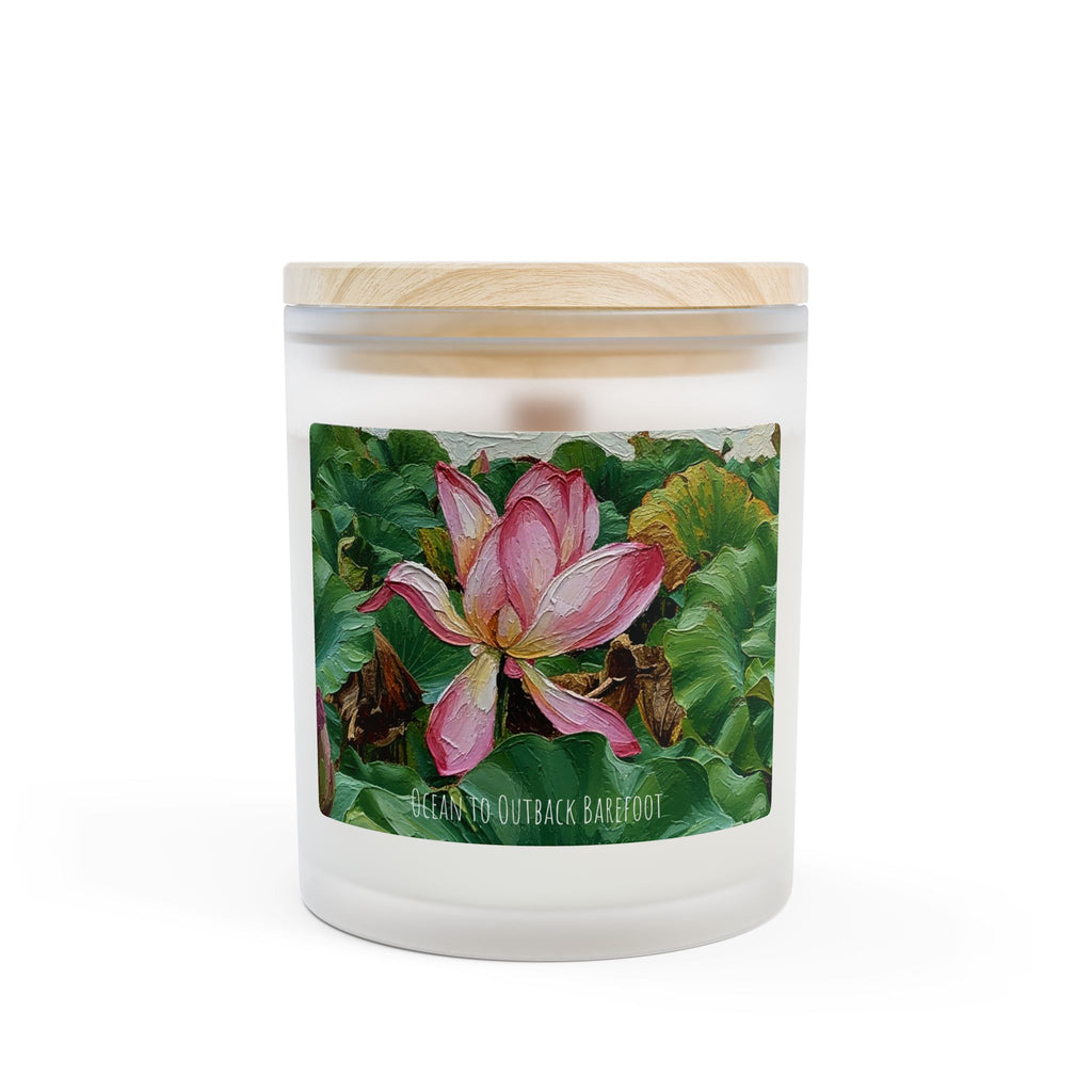 A frosted glass jar candle with a light wood lid, featuring a label with a pink lotus flower on green lily pads. The text 'OCEAN TO OUTBACK BAREFOOT' is printed on the label.