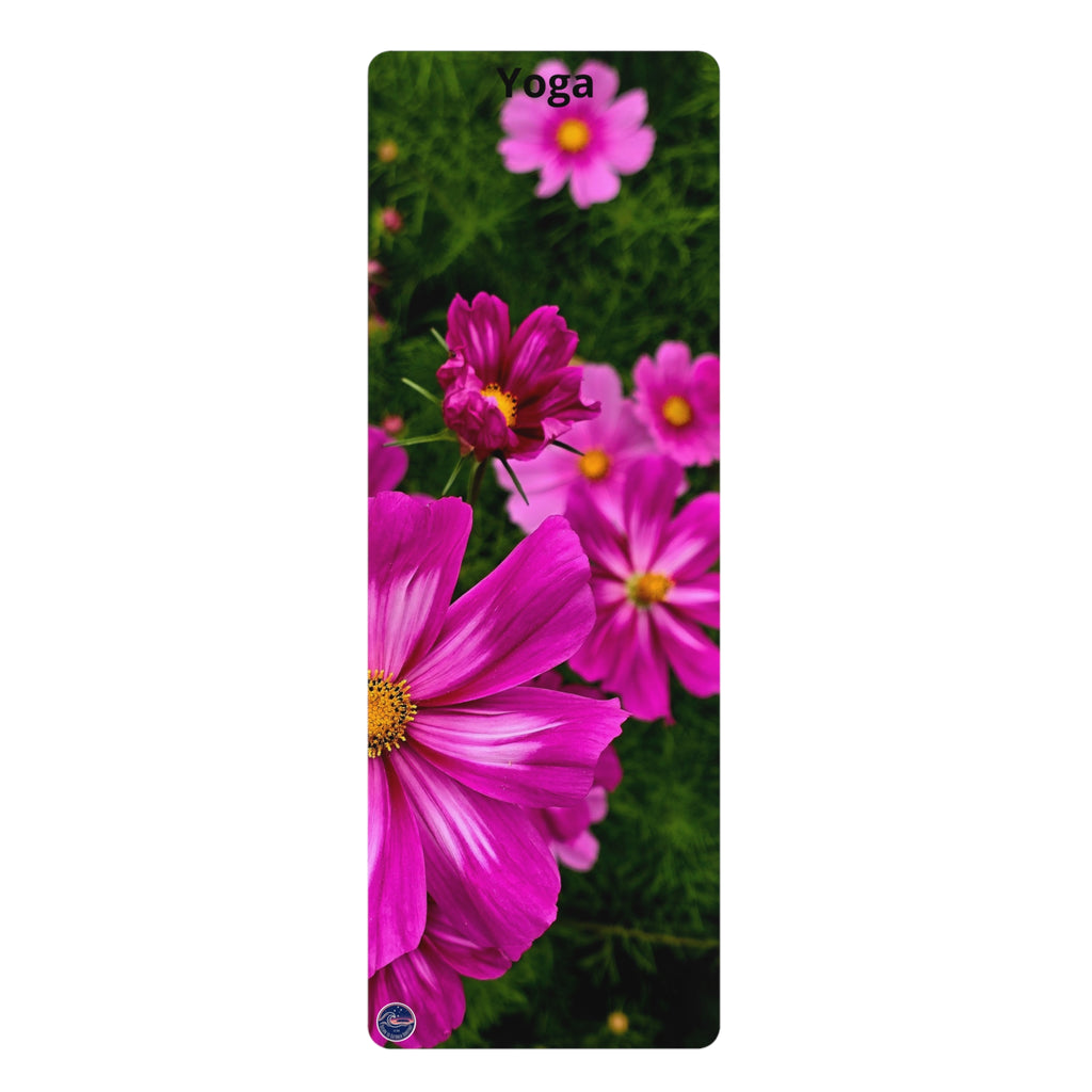 A vertical yoga mat featuring a vibrant print of pink cosmos flowers with yellow centers against a dark green leafy background. The word 'Yoga' is printed in black at the top, and a small circular blue logo is at the bottom left.