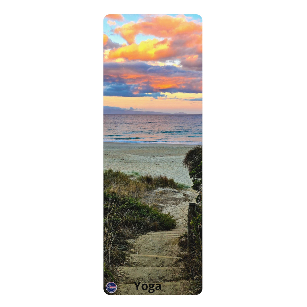 A tall rectangular yoga mat featuring a scenic beach landscape print with a sunset sky, ocean, dunes, and a stone path. The word 'Yoga' is printed near the bottom, and a small circular logo appears in the lower left corner.