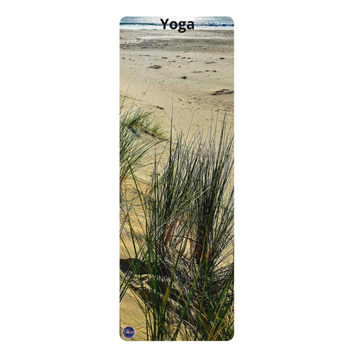 A yoga mat featuring a scenic photograph of beach dunes with sand, sea oats, and a distant ocean under a blue sky. The word 'Yoga' is printed at the top, and a small circular logo is in the bottom-left corner.