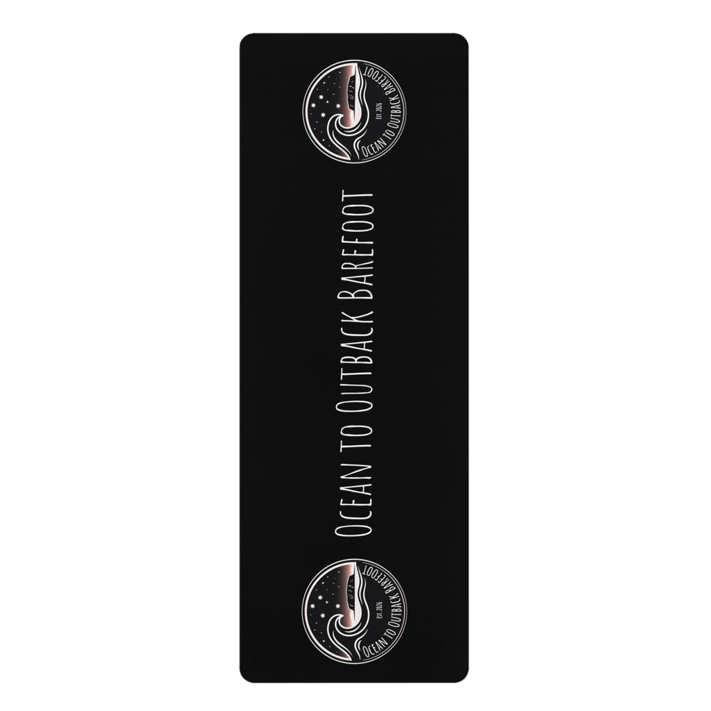 A black rectangular yoga mat with rounded corners, featuring the text 'OCEAN TO OUTBACK BAREFOOT' in white vertical lettering, flanked by two circular logo designs at the top and bottom on a white background.
