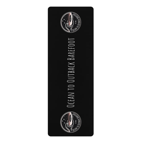 A black rectangular yoga mat with rounded corners, featuring the text 'OCEAN TO OUTBACK BAREFOOT' in white vertical lettering, flanked by two circular logo designs at the top and bottom on a white background.